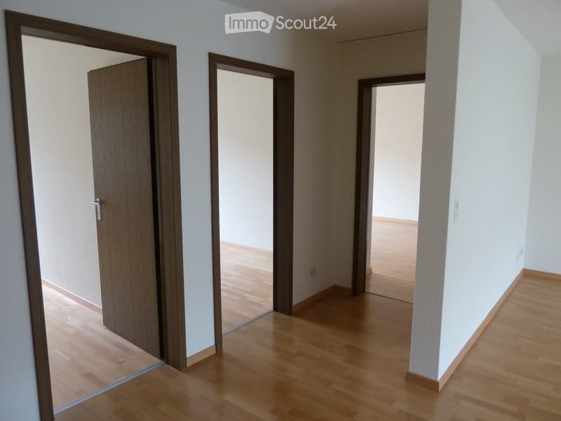Empty hallway with light wooden flooring, white walls, and multiple doors leading to other rooms.