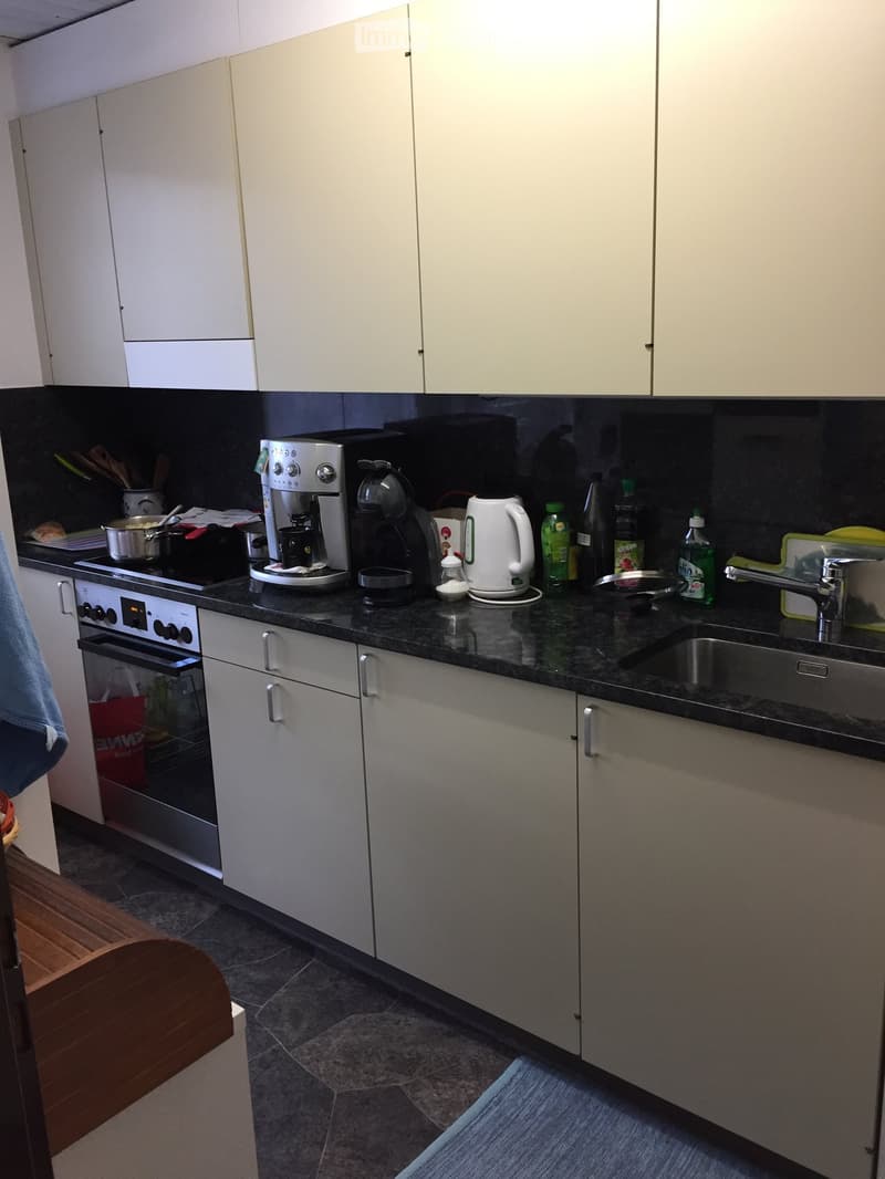 Modern kitchen with white cabinets, black countertops, stainless steel appliances, and various kitchen items on the counter.