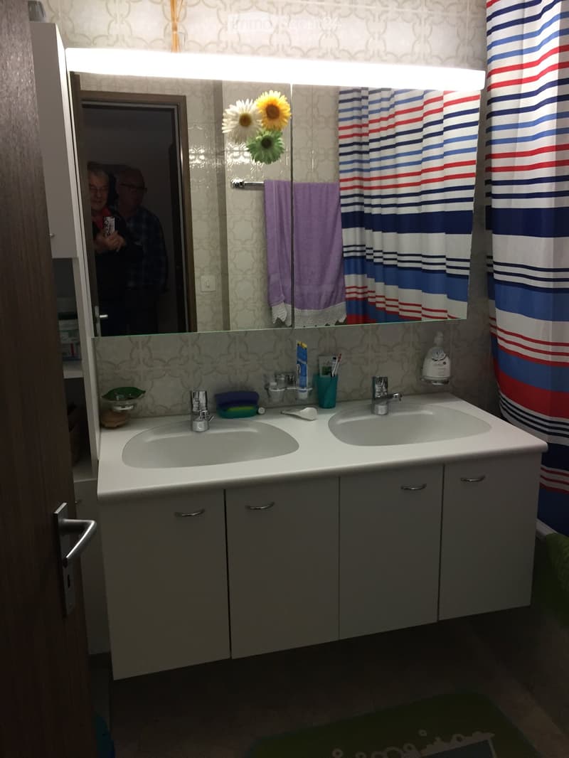 Bathroom with double sink, mirrored cabinet, shower curtain, and various toiletries.