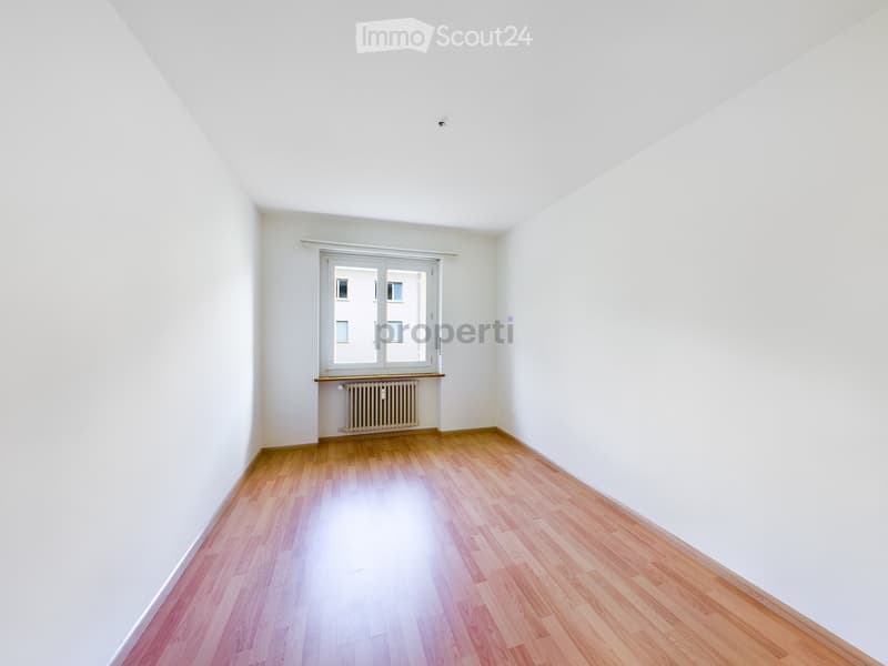 Empty room with white walls, wooden flooring, and a window with a radiator below it.