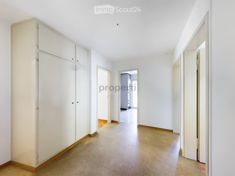 Empty hallway with white walls, tiled floor, and built-in storage unit on one side. Doors lead to other rooms.