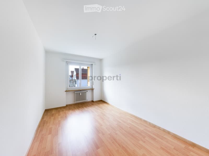 Empty room with white walls, wooden flooring, and a window with a radiator below it.