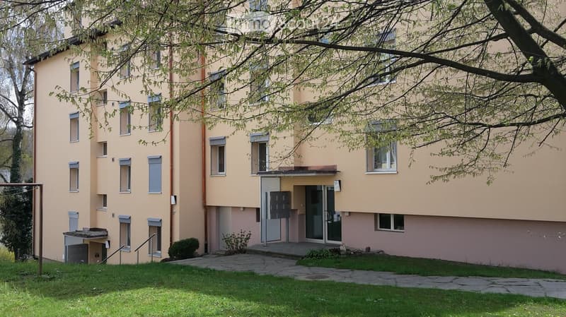Four-story residential building with light yellow facade, multiple windows, and a small entrance area with steps and a small garden.