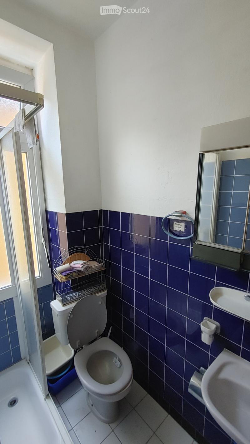 Small bathroom with blue tiled walls, white tiled floor, toilet, sink, mirror, and a towel rack with towels.