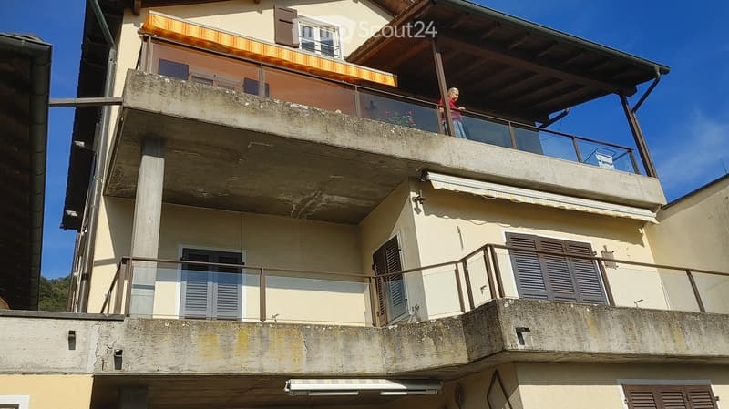 Two-story residential building with balconies, shutters, and awnings.