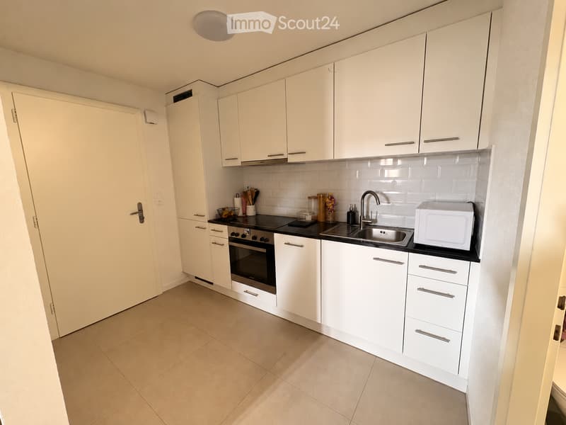 Modern kitchen with white cabinets, stainless steel sink, microwave, and oven. Features a tiled backsplash and tiled floor.
