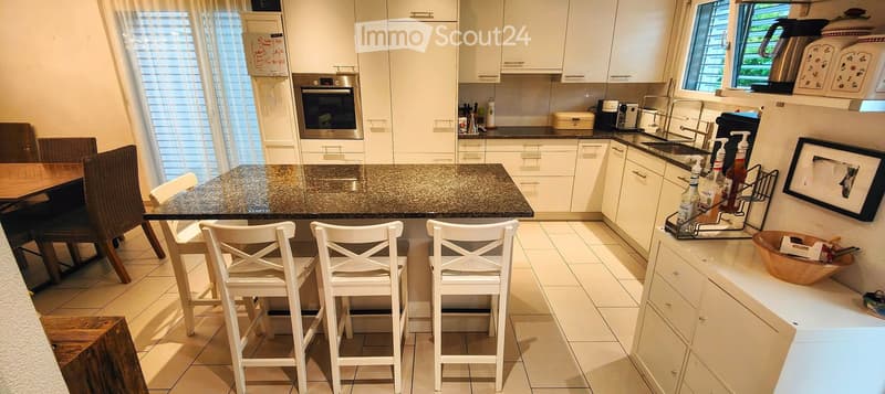 Modern kitchen with white cabinets, granite countertop, island with bar stools, and various appliances including an oven and sink.