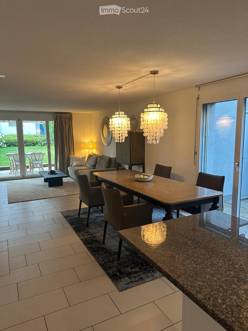 Open-plan living and dining area with a sofa, coffee table, dining table, chairs, and decorative lighting.