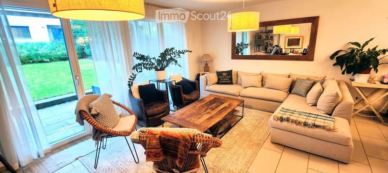 Bright living room with large windows, a beige sectional sofa, wooden coffee table, wicker chairs, and decorative pillows.