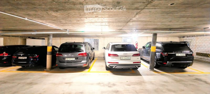Underground parking area with several parked cars, concrete pillars, and yellow parking lines.