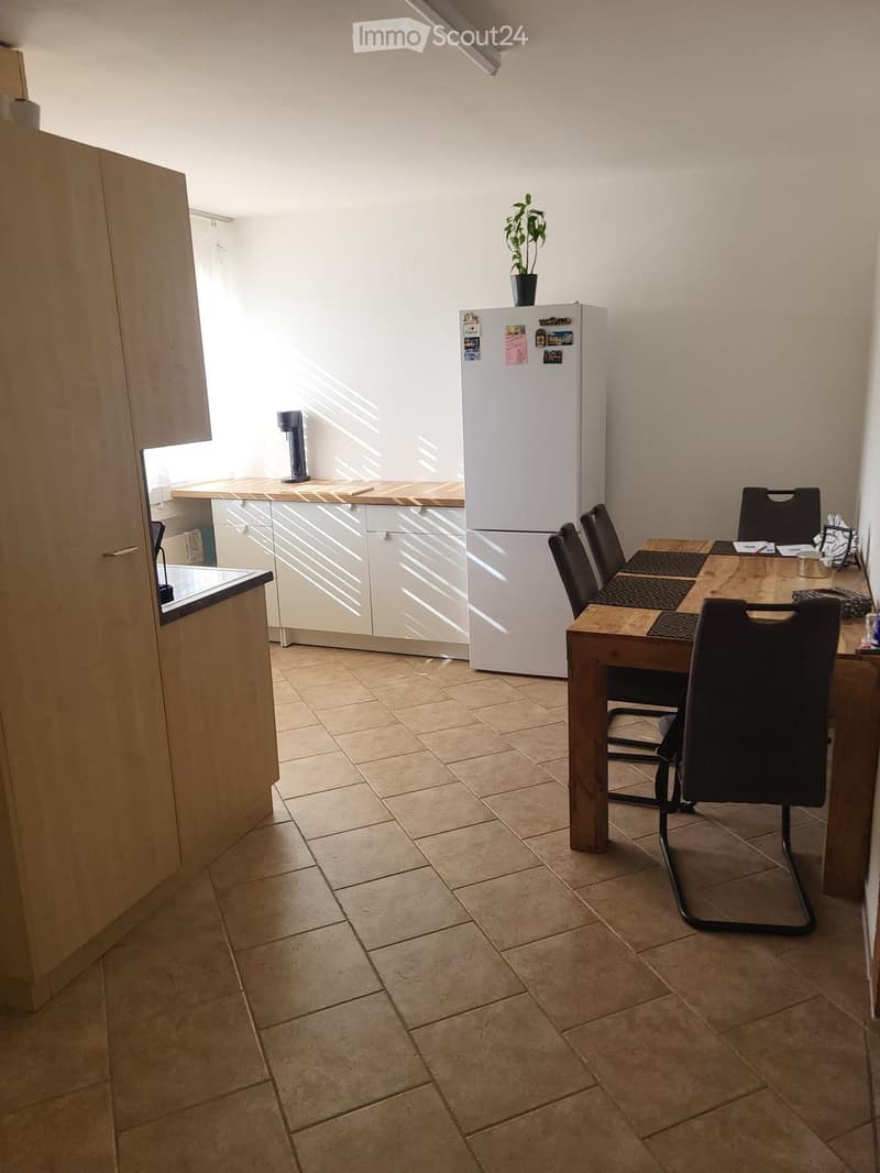 A modern kitchen and dining area with a refrigerator, a wooden dining table, chairs, and a cabinet.