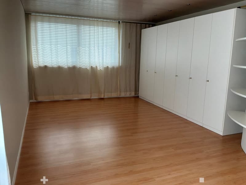 Empty room with wooden flooring, white built-in wardrobes, and a window with beige curtains.