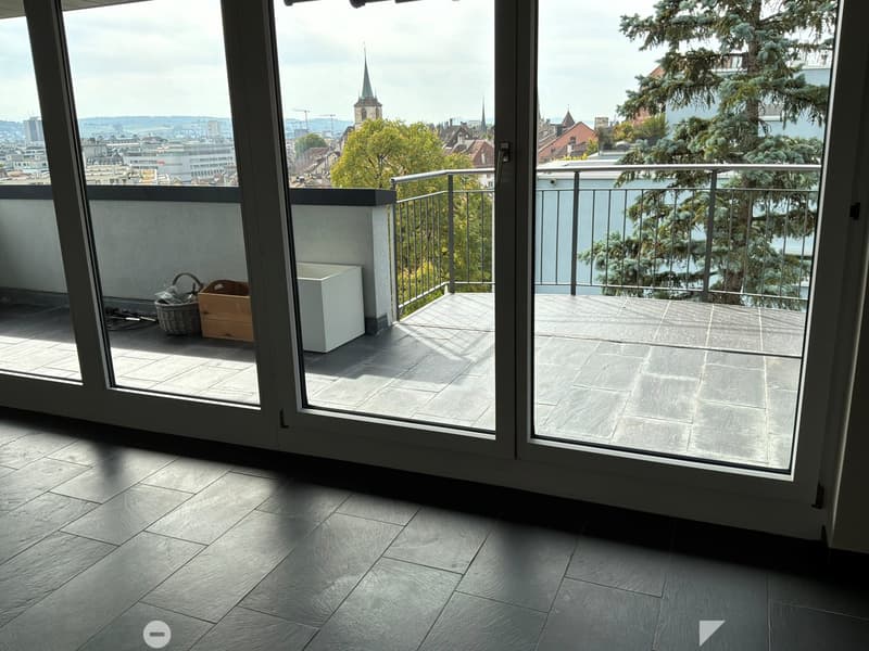 Balcony with tiled flooring, metal railing, and scenic city view. Contains a wicker basket, wooden crate, and white cabinet.