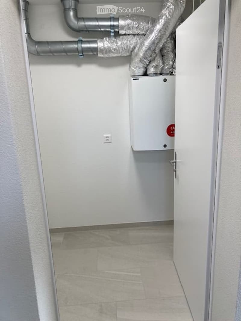 Utility room with white walls, tiled floor, and exposed pipes. A white electrical panel is mounted on the wall.