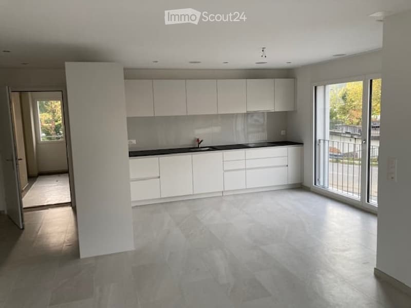 Modern, minimalist kitchen with white cabinets, a central island, and a large window offering a view of the outdoor area.