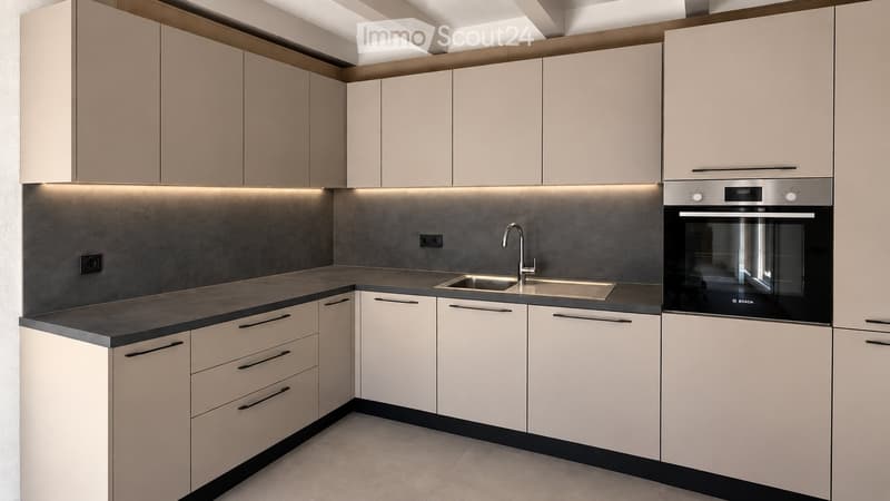 Modern kitchen with light-colored cabinets, dark countertops, and built-in appliances including a sink and oven.