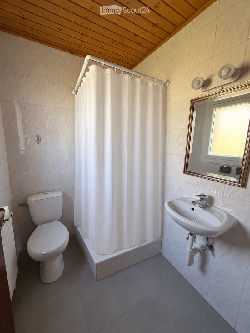 Clean bathroom with white tiles, a toilet, a sink, a mirror, and a shower curtain.