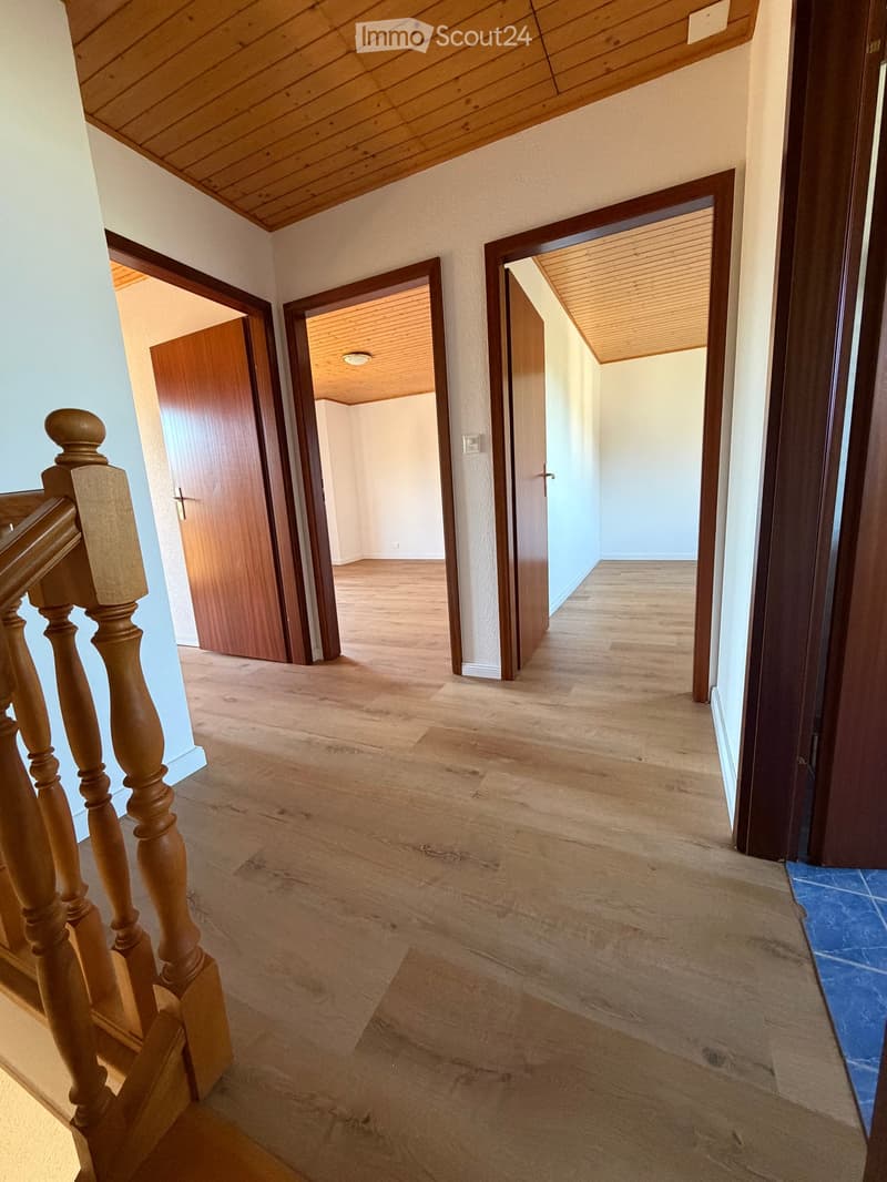 Empty hallway with wooden flooring, wooden doors, and a staircase with wooden railings. The ceiling is wooden with recessed lighting.