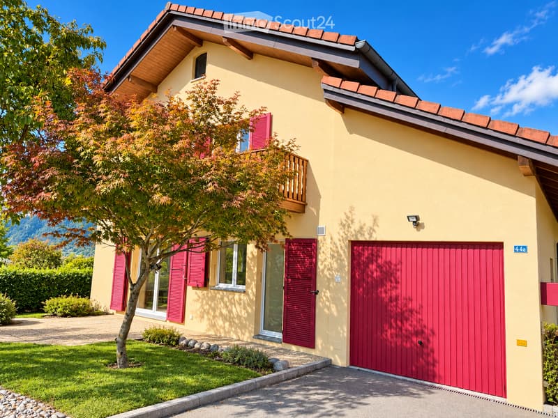 Two-story house with yellow exterior, red shutters, garage, and balcony overlooking a garden area.