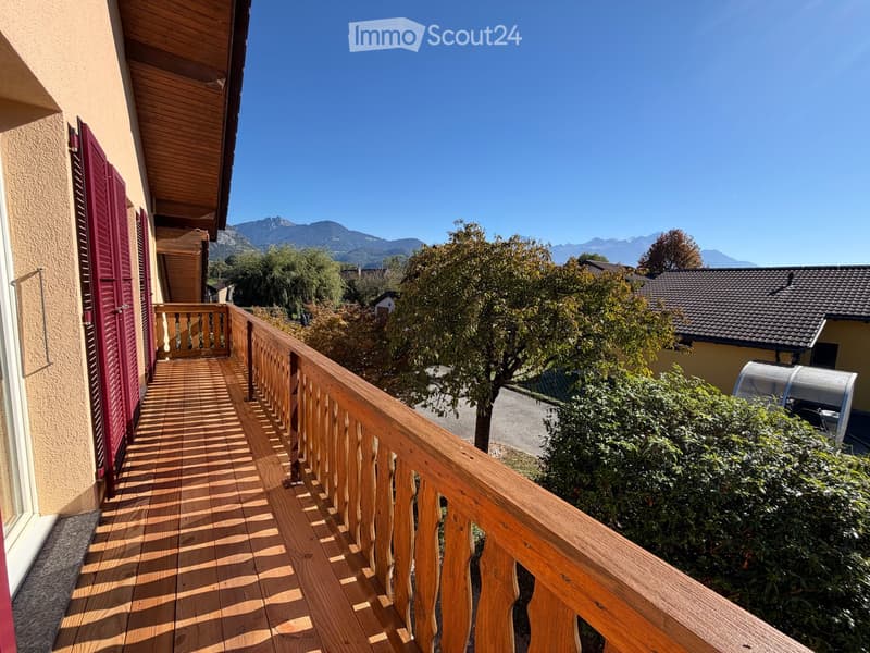 Wooden balcony with wooden railing, overlooking a scenic mountain view and surrounding greenery.