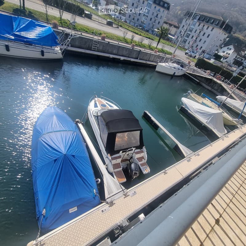 Marina with several boats docked, including a sailboat and motorboats, with covered hulls and a calm water surface.