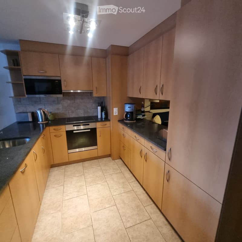 Modern kitchen with light wooden cabinets, stainless steel appliances, and granite countertops.
