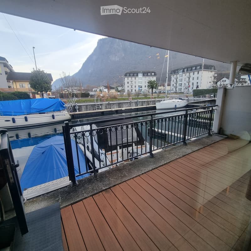 Balcony with wooden decking, black metal railing, overlooking a harbor with boats and a mountain view.
