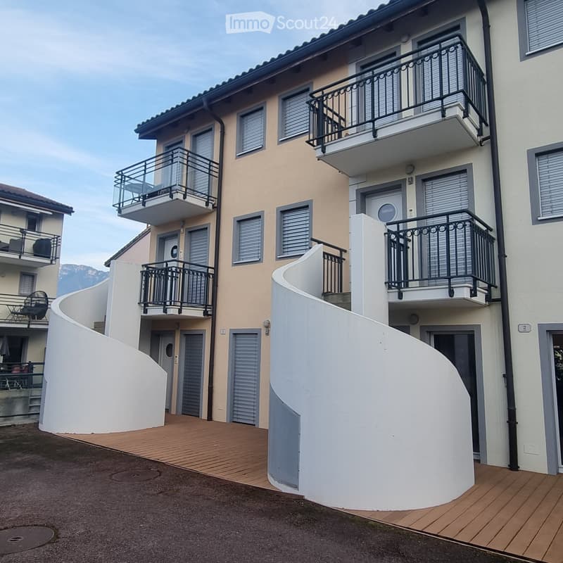 Modern two-story building with beige facade, multiple balconies with black railings, and a wooden deck area.