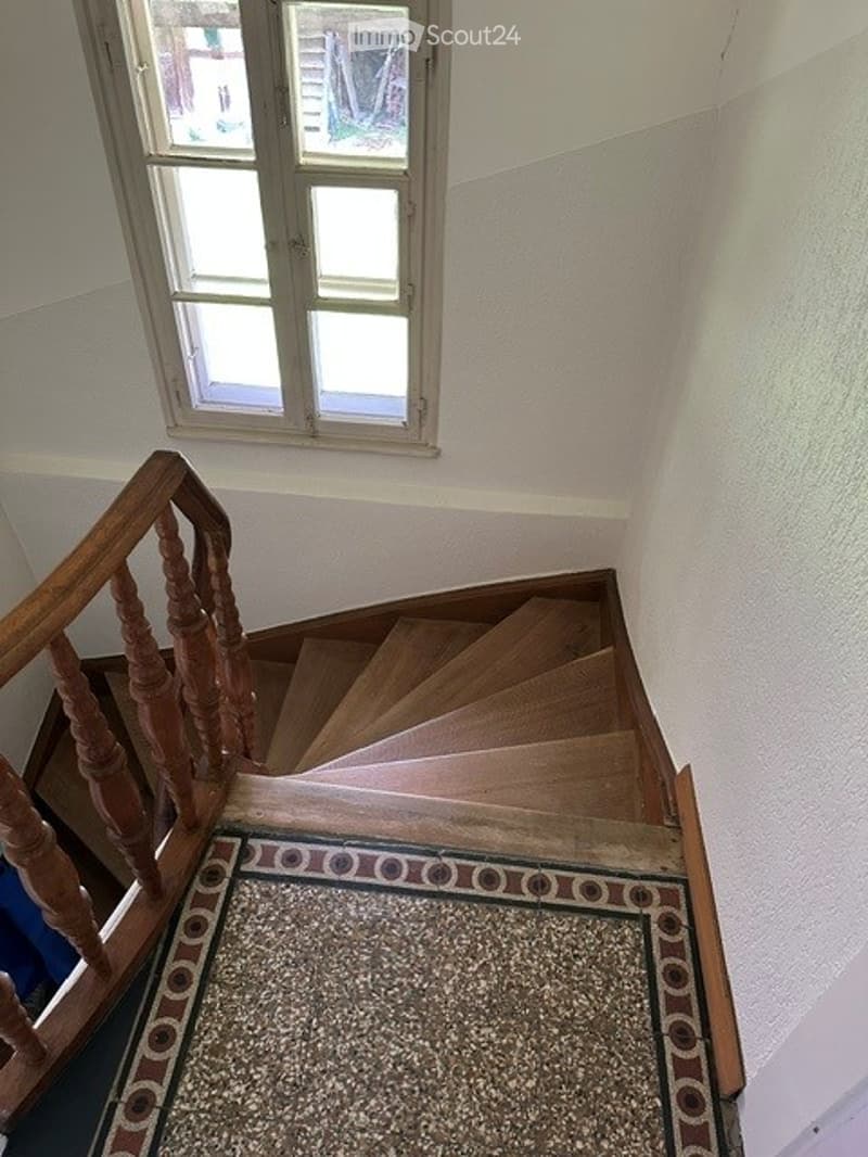 Wooden staircase with a decorative runner and a window at the top, leading upwards.