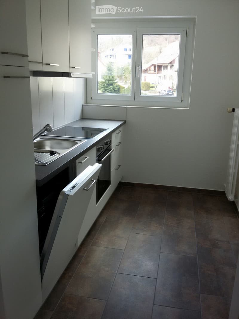 Modern kitchen with white cabinets, stainless steel sink, oven, and tiled floor. Large window offers a view of the street.