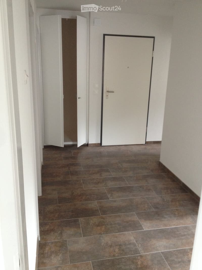 Empty hallway with tiled floor and white walls, featuring two closed doors and a visible light switch.