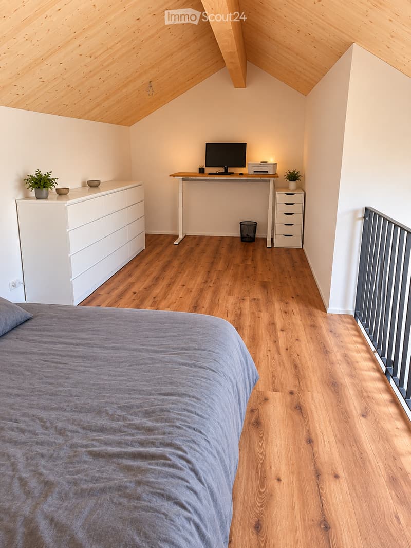 Cozy bedroom with a wooden slanted ceiling, hardwood floor, and modern furnishings including a bed, desk, dresser, and small potted plants.