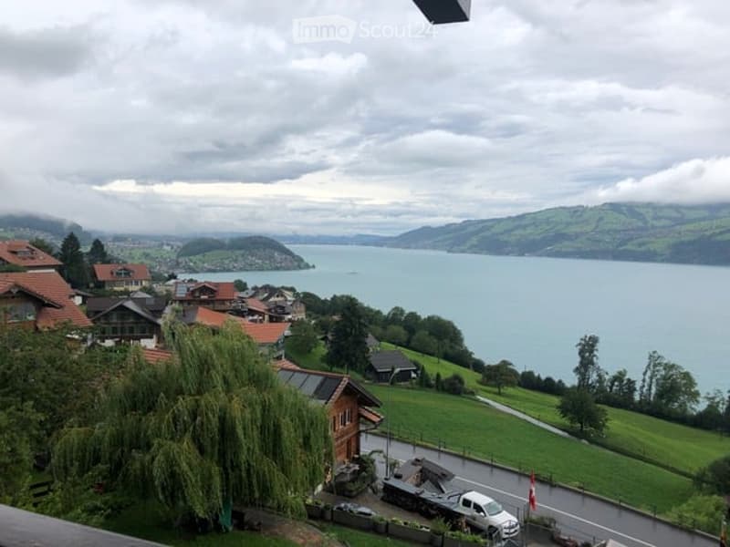 Panoramic view from a balcony overlooking a serene lake surrounded by green hills and scattered houses.
