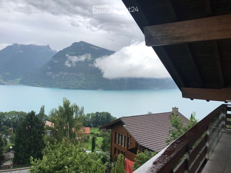 Balcony overlooking a scenic lake and mountain landscape with a wooden railing and tiled floor.