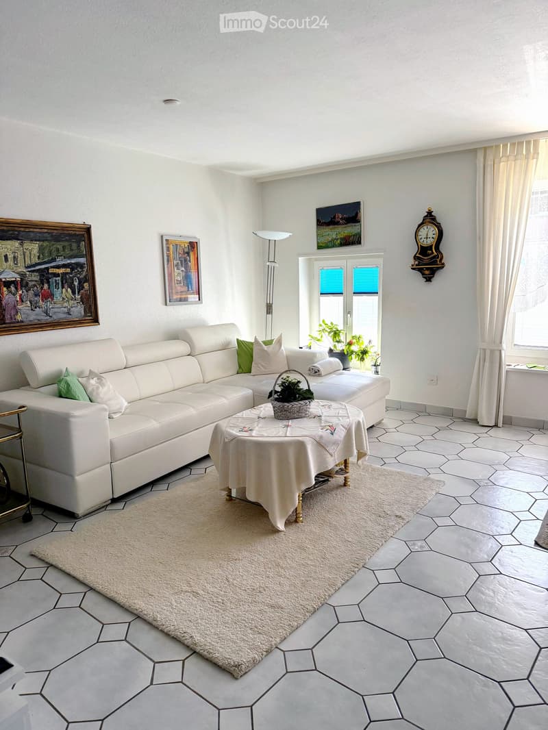 Bright living room with white walls, hexagonal tile floor, white sectional sofa, coffee table with a basket, floor lamp, and artwork on the walls.