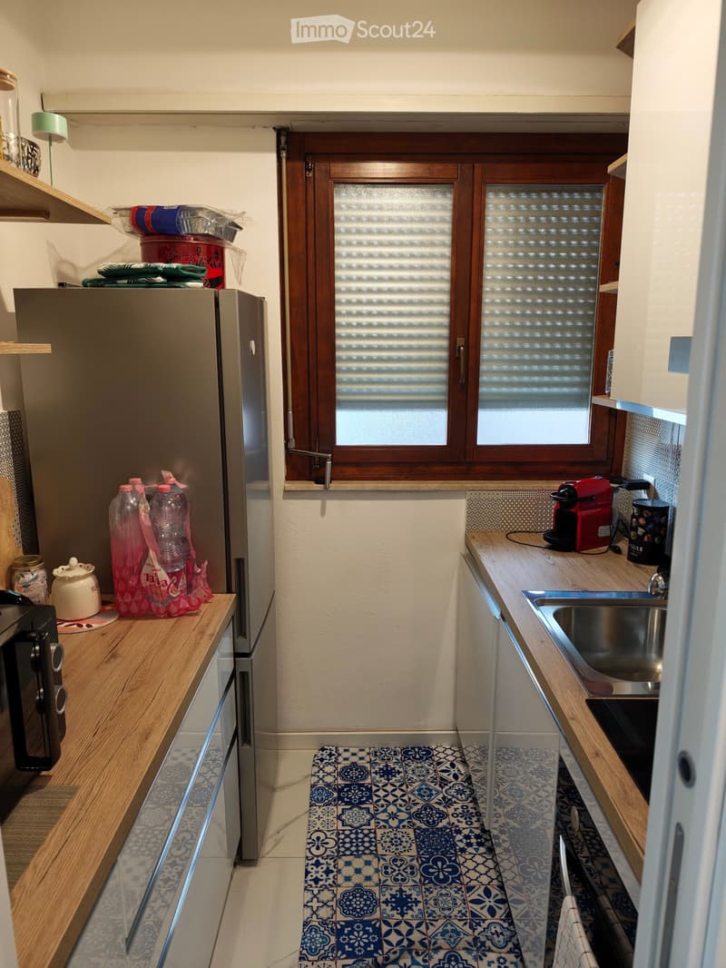 Compact kitchen with wooden countertops, stainless steel sink, refrigerator, microwave, coffee maker, and various small items on the counters.