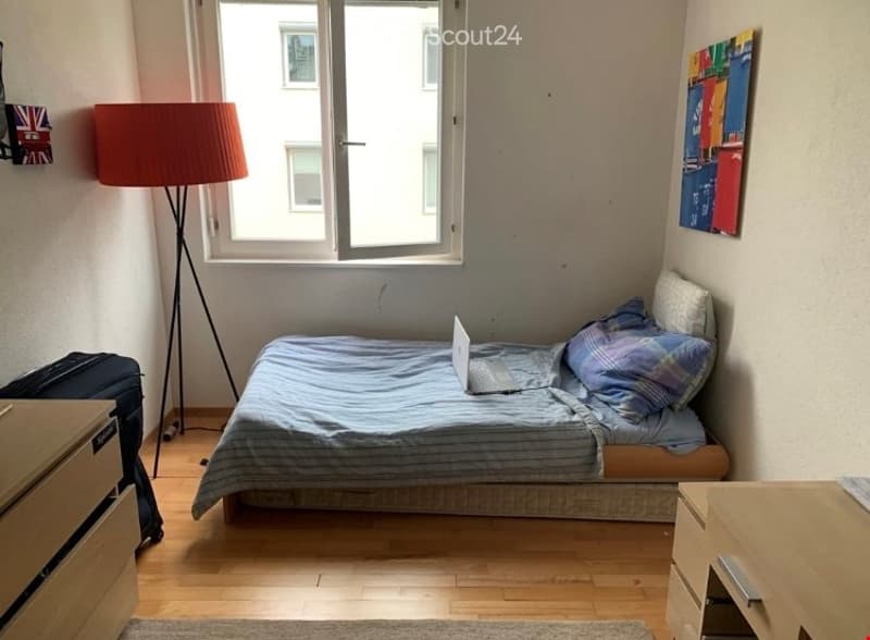 Cozy bedroom with a single bed, laptop on the bed, floor lamp, nightstand, and a picture frame on the wall.