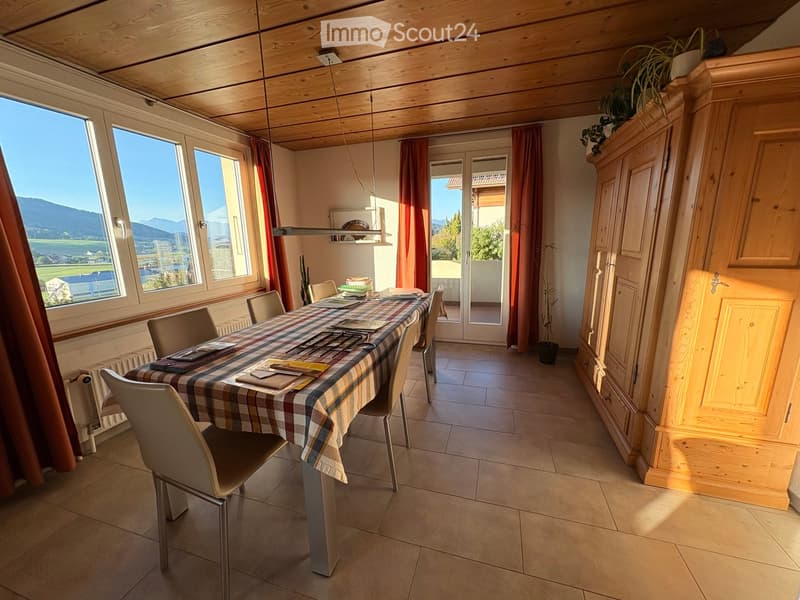 Bright dining room with large windows offering a scenic mountain view, a wooden ceiling, a dining table with chairs, and a tall wooden cabinet.