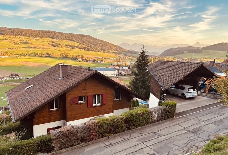 Two-story wooden house with red shutters, garage, and scenic mountain view.