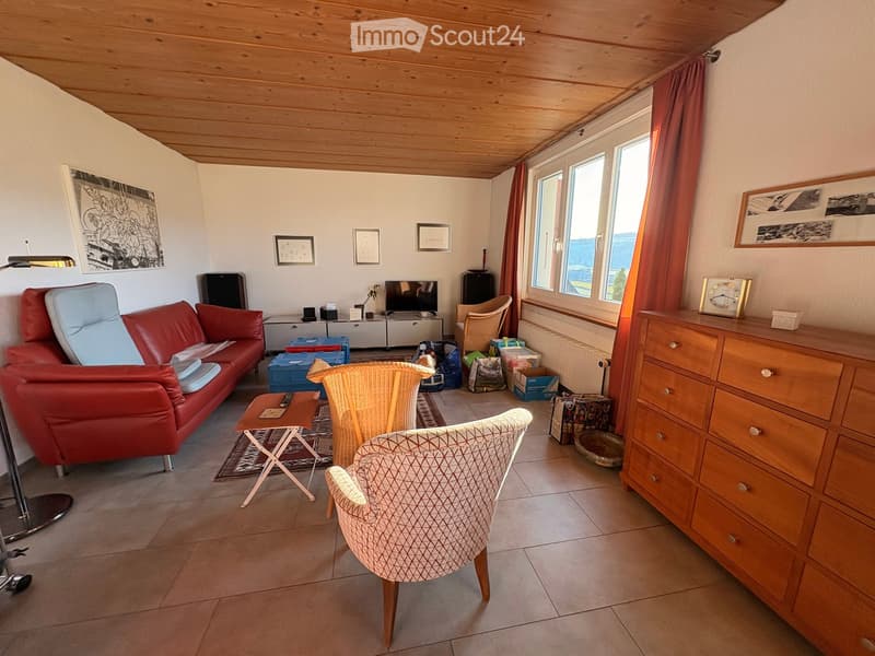 Living room with a red leather sofa, wicker chairs, a small wooden table, a television, and a wooden cabinet with drawers.