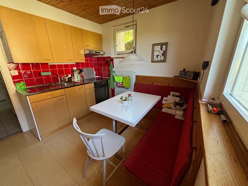 Cozy kitchen with wooden cabinets, red tiled backsplash, white table and chair, and a red bench seating area.