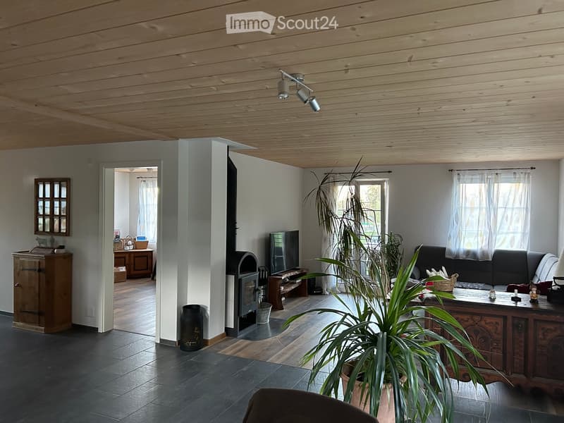 Modern living room with a fireplace, large windows, and a sofa, coffee table, and television. Wooden ceiling and tiled floor.
