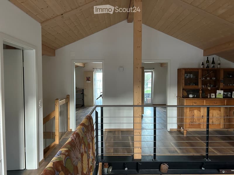 Modern hallway with wooden beams, glass railing, and open wooden shelving unit with decorative items and bottles.