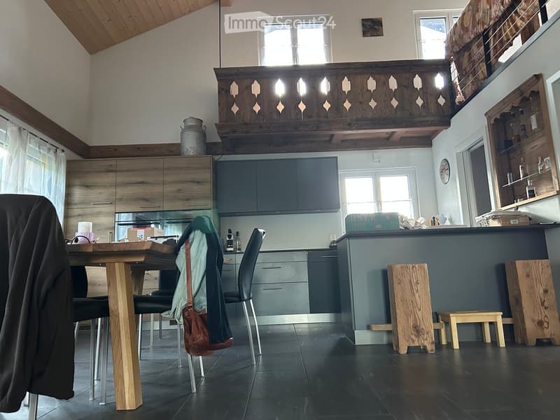 Modern kitchen with wooden table, chairs, stools, grey cabinets, and a wooden balcony railing above.