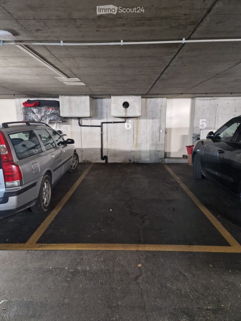 Underground parking area with two parked cars, marked parking spaces, and concrete walls.