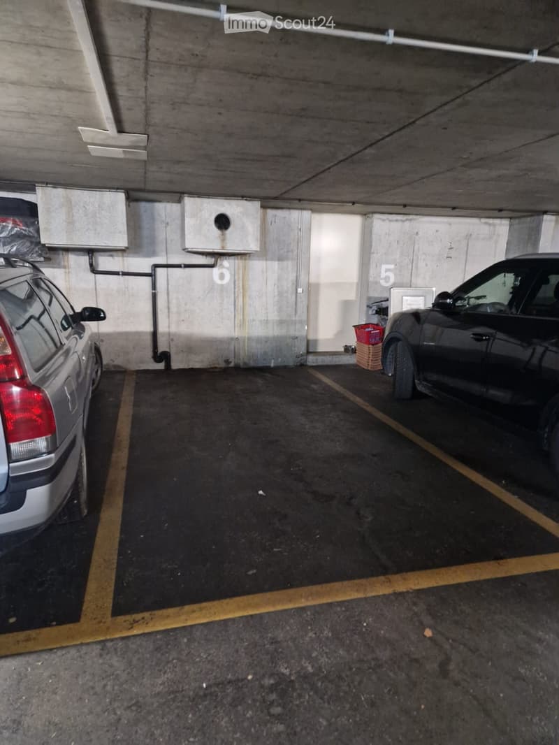 Underground parking area with two parked cars, marked parking spaces, and numbered sections.