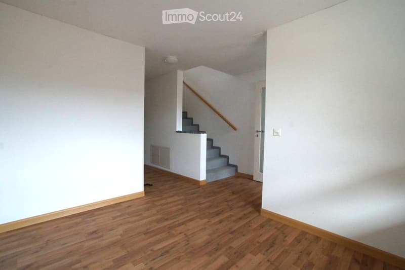 {"type": "Room", "description": "Empty room with hardwood floors, white walls, a central staircase, and a door at the end.", "visible_features": []}