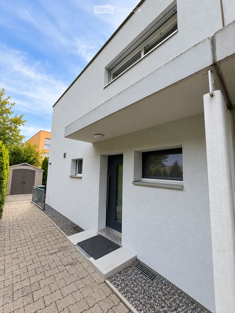 Modern two-story house with white exterior, large windows, and a raised ground floor entrance.