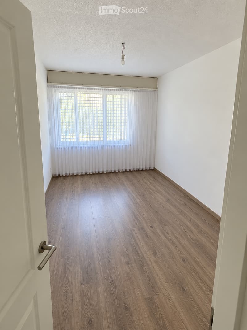 Empty room with wooden flooring, white walls, and a window with sheer curtains. No furniture or equipment present.