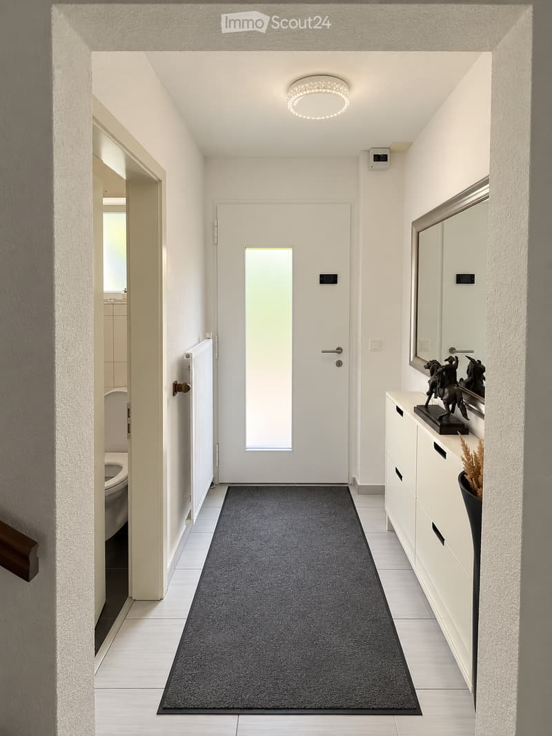 Modern hallway with white walls, grey carpet runner, white tiled floor, and a small cabinet with decorative items on top.